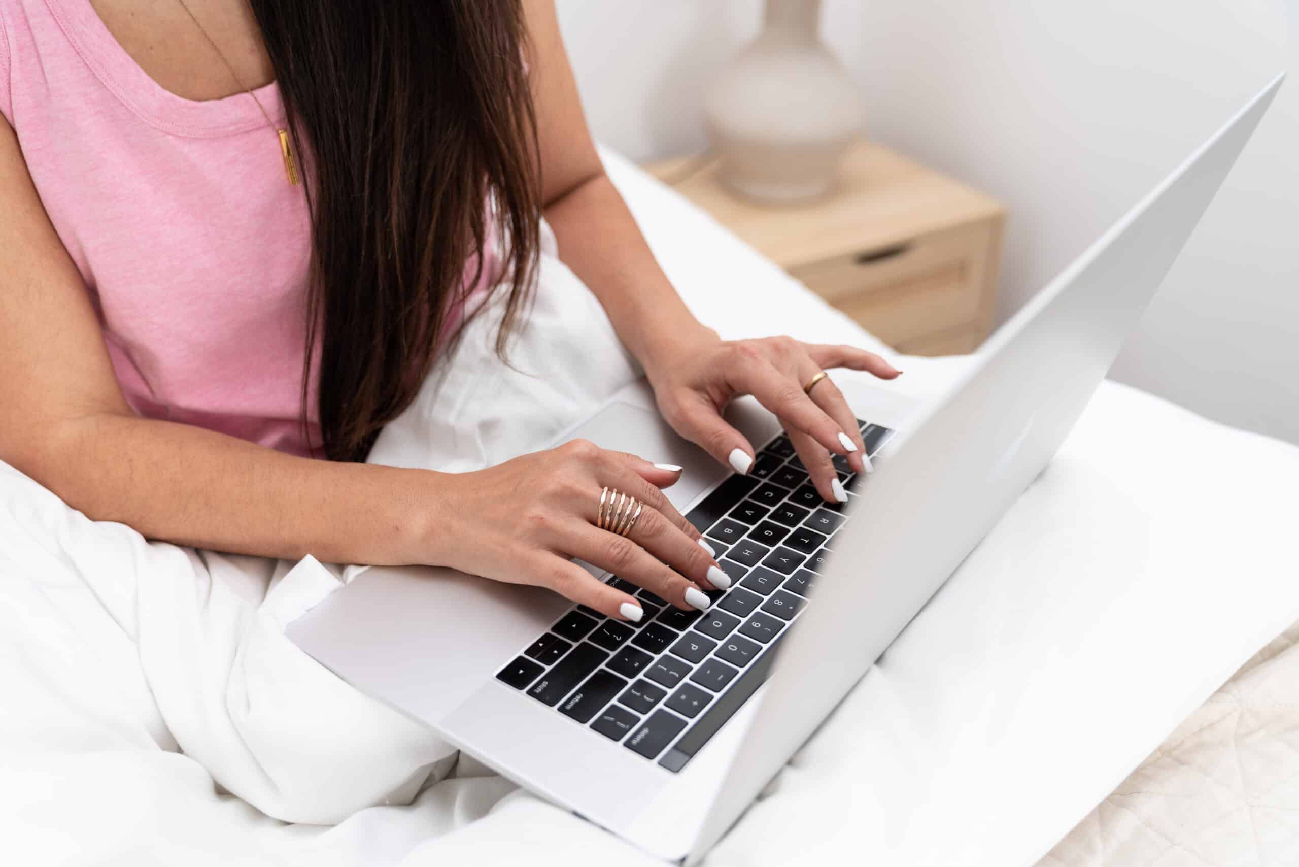 An accomplished web designer effortlessly typing away on her laptop in the comforts of her bed, equipped to build a stunning website for clients on the Gold Coast.