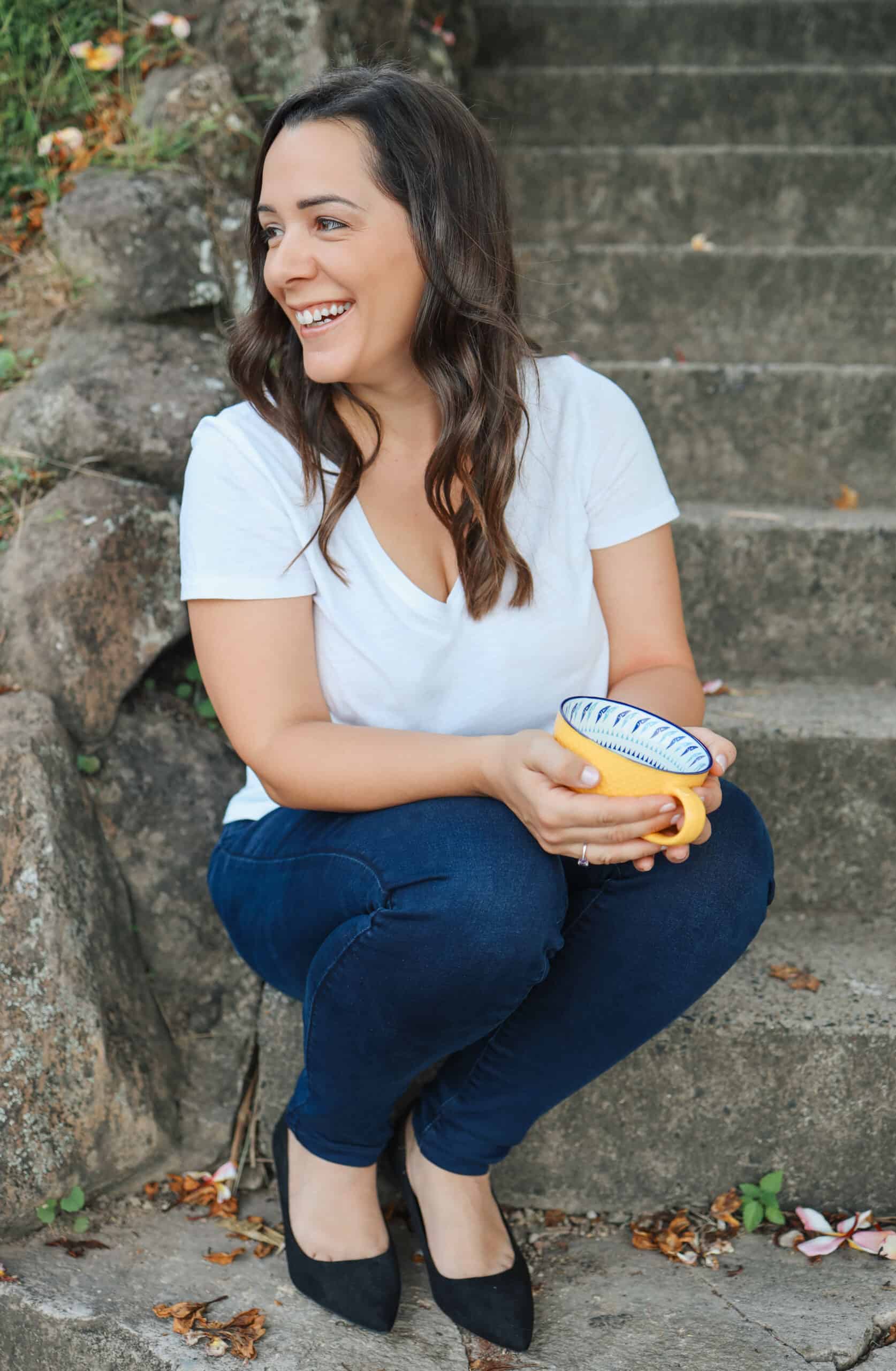 A woman sitting on steps, stylishly holding a yellow cup.