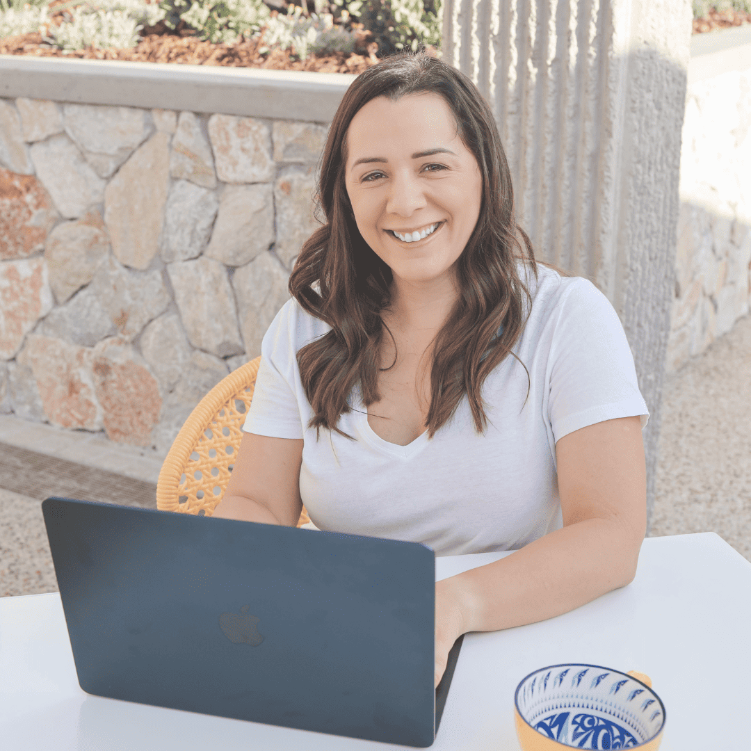 a smiling woman sitting at a table with a laptop, browsing through website policies.